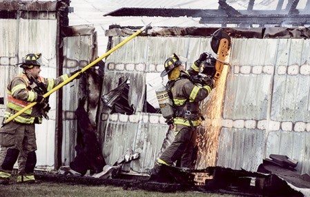 An Austin firefighter cuts away a section of wall of a shed that burned at 1703 20th Street SW Monday evening. Eric Johnson/photodesk@austindailyherald.com