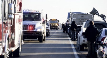 A convoy of emergency vehicles lead the football team north out of town on County Road 8. 