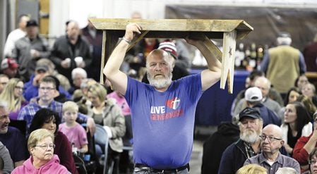 Tom Lewiston carries a bench being bid on during the Lyle Area Cancer Auction Friday night. Eric Johnson/photodesk@austindailyherald.com